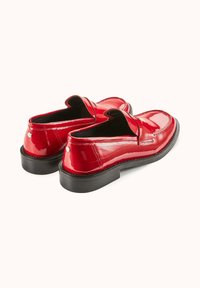 Mocassins en cuir verni rouge avec une finition lisse, semelle noire basse et couture décorative au niveau des orteils et sur les côtés. Forme arrondie et style à enfiler.