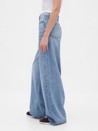 Person wearing light blue wide-leg jeans, white top, and dark brown sneakers against a plain white background.