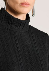 Schwarzer Rollkragenpullover mit strukturiertem Zopfmuster, hoher Kragen und gerippten Akzenten. Nahaufnahme des Halsbereichs.