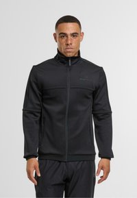 Černá zipová bunda z měkké látky, s vysokým límcem, bočními panely a diskrétním logem na prsou. Hladká textura a přiléhavý střih.
