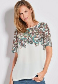 Lichte, crèmekleurige blouse met kleurrijke paisley borduursels op de halslijn en mouwen. Ronde hals, korte mouwen en een losse pasvorm.