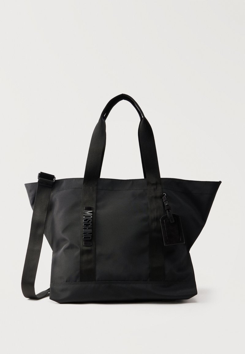 Μαύρη τσάντα tote από νάιλον με δύο πάνω λαβές, ρυθμιζόμενο λουρί ώμου και μικρή προσαρτημένη ετικέτα, με κάθετο κείμενο MOSCHINO μπροστά.