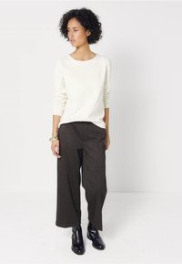 Witte lange mouwen trui, donker gepatternde wijde broek en zwarte enkellaarsjes. Strakke lijnen met een ontspannen pasvorm door het hele outfit.