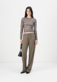 Langarmtop in doorschijnend beige met een zwart zebra patroon, gecombineerd met olijfgroene wijde broek en puntige zwarte schoenen.