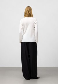 Maglietta bianca a maniche lunghe con una consistenza liscia abbinata a pantaloni neri larghi, caratterizzati da un design fluido e aperture ampie sulle gambe.