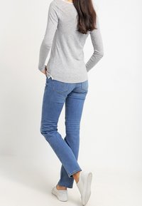 Maglietta grigia a maniche lunghe con spacchi laterali abbinata a jeans blu a gamba dritta. L'outfit è completato da sneakers bianche.