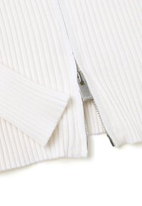 Cardigan bianco a coste con zip frontale, dotato di una cerniera argentata e una texture morbida. Maniche e orlo presentano un motivo a coste uniforme.