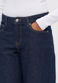 Mörka denimjeans med ljusa sömmar, hög midja, framfickor och metallknapp stängning. Mjuk textur med rak passform.