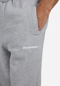 Grijze sweatpants met een zachte textuur, voorzien van een zijzak en een geborduurd "PEGADOR" logo in het wit op het linkerbeen.