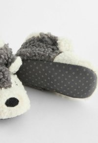 Chaussons en peluche gris et blanc avec un extérieur texturé, un bout rond et une semelle en caoutchouc à points pour une meilleure adhérence. Le design supérieur est constitué d'un tissu doux.