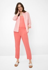 Koraalroze shirt met witte strepen, gecombineerd met bijpassende koraalbroeken en beige sandalen. Lichtgewicht stof, ontspannen pasvorm, casual stijl.