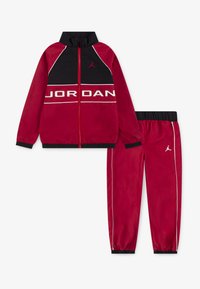 Das rote und schwarze Trainingsanzug-Set umfasst eine Zip-Jacke mit dem Schriftzug "JORDAN" und passende Hosen mit elastischen Bündchen und weißen Akzentlinien.