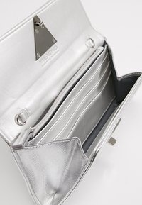 Silverfärgad metallplånbok med ett triangulärt silverfärgat spänne. Har flera kortfack och ett zip-fodrat fack. Texturerad insida.