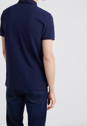 Polo azul marino de manga corta con cuello clásico. La tela parece suave con una textura sutil, combinado con jeans de mezclilla oscura.