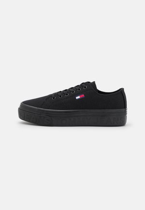 Sort lavt canvas-sneaker med sort sål præget med "Tommy Jeans" og lille rød, hvid og blå flaglogo på siden.