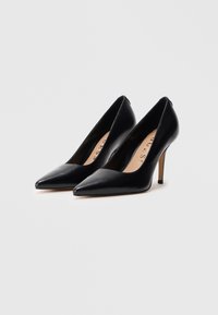 Escarpins en cuir noir avec un bout pointu, un talon aiguille fin, une texture lisse et un design minimaliste. Logo de la marque discret sur la semelle intérieure.