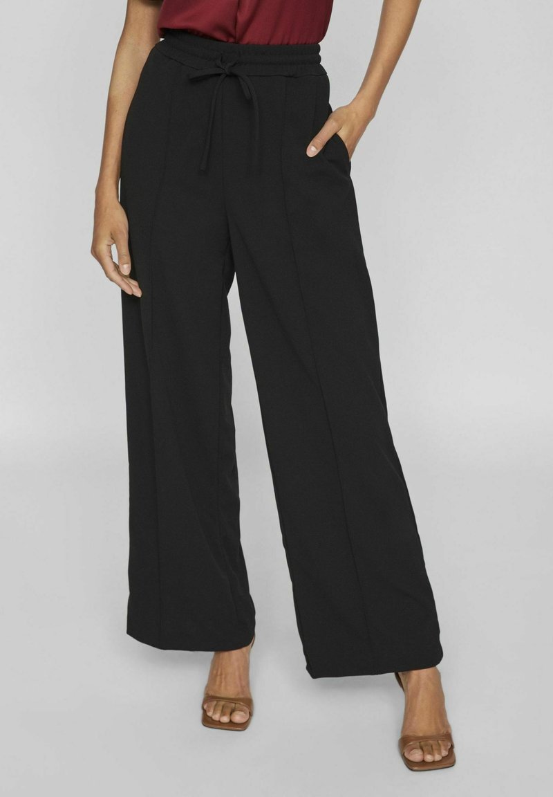 Pantalons larges noirs avec une taille élastique et un cordon de serrage, dotés de poches latérales, d'un design raffiné et d'une texture de tissu lisse.