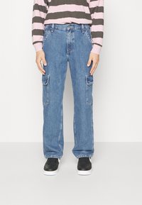 Ljusblå cargojackor med två sidofickor, en figurnära midja, vida ben och en något sliten yta. Bärs med svarta sneakers.