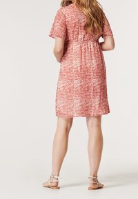 Röd och gräddfärgad mönstrad klänning med korta ärmar, markerad midja och knälång fåll. Bärs med beiga sandaletter med remmar.