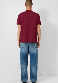 Bordo pamučna majica s kratkim rukavima i okruglim izrezom, u kombinaciji s oversized svijetloplavim trapericama koje imaju izbledele dijelove i stražnje džepove.