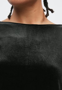 Top em veludo preto com um decote largo, apresentando uma superfície lisa e texturada com detalhes mínimos. O tecido parece macio e luxuoso.