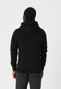 Sudadera negra con capucha ajustable, puños y dobladillo acanalados. Textura suave con un acabado uniforme, que exhibe un diseño simple y moderno.