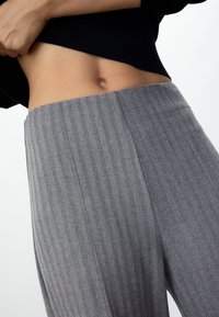 Grijze broek met ruitpatroon, hoge taille en een gladde textuur. De stof heeft een subtiele glans en valt licht.