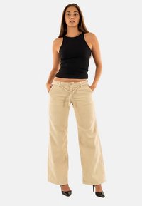 Beige wijde broek met steekzakken aan de voorkant, een knoopsluiting en riemlussen, gecombineerd met een aangesloten zwart tanktopje.