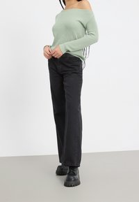 Vaaleanvihreä ribattu olan paljastava neule, yhdistetty mustiin korkeavyötäröisiin farkkuihin ja mustiin paksupohjaisiin nyörikenkiin. Yksinkertainen, rento kokonaisuus.