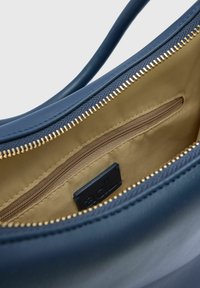 Blauwe leren handtas interieur met gouden rits, beige voering en een klein ritsvakje. Merkenlabel zichtbaar binnenin.