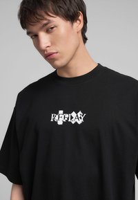 T-shirt nera in cotone con maniche corte, con un logo "REPLAY" bianco e consunto ricamato sul davanti. Collo tondo, vestibilità comoda.