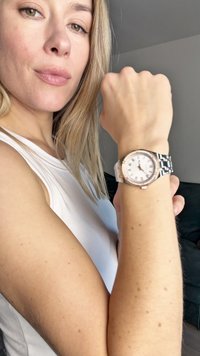 Sølv- og rosaguldur med en rund hvid urskive, romerske tal og et metalarmbånd, båret på en lys hudfarvet arm.