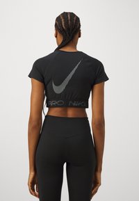 Camiseta negra cortada de Nike con mangas cortas, que presenta un logo de swoosh blanco y texto en el dobladillo, combinada con leggings negros de cintura alta.