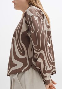 Brown and beige long-sleeve shirt with a wavy pattern, made of lightweight fabric, featuring a rounded hem and buttoned cuffs.