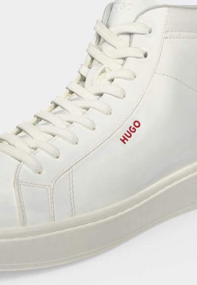 Baskets montantes blanches avec lacets blancs, logo rouge "HUGO" sur le côté et coutures détaillées sur cuir lisse.