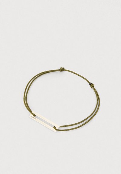 Podesivi narukvica od maslinasto zelene pletene cord trake s horizontalnom pravokutnom srebrnom metalnom šipkom ugraviranom s "le gramme" na bijeloj pozadini.