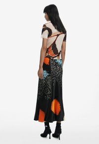 Jupe maxi multicolore avec un motif floral en orange, bleu et noir, présentant une fente haute. Le matériau semble soyeux et lisse.