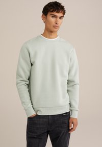 Mint green sweatshirt with a crew neckline, long sleeves, and ribbed cuffs. Soft texture and relaxed fit, paired with dark denim jeans.