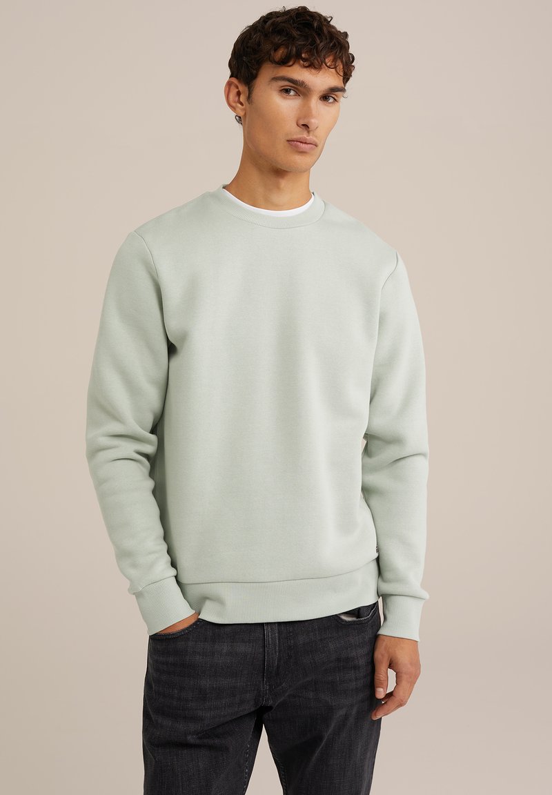 Mint green sweatshirt with a crew neckline, long sleeves, and ribbed cuffs. Soft texture and relaxed fit, paired with dark denim jeans.