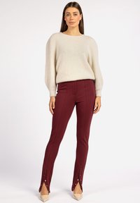 Romantisch crèmekleurig fuzzy sweater met brede mouwen, gecombineerd met aangesloten bordeauxrode broek met zijbutton-details en een naadloze textuur.