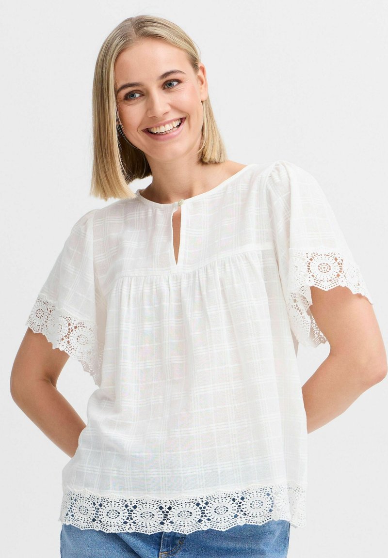 Blusa bianca con maniche corte rifinite in pizzo e scollatura a keyhole. Il tessuto texturizzato presenta un leggero motivo a griglia.