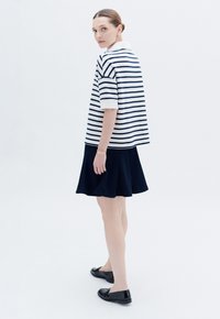Polo a righe a maniche corte in bianco e blu navy, abbinato a una gonna blu navy fino al ginocchio. Scarpe nere slip-on completano l'outfit.