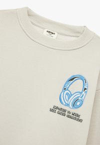 Lichtgrijze sweatshirt met een blauw geborduurd hoofdtelefoonontwerp en de tekst "Blootstelling aan muziek zal creativiteit veroorzaken" daaronder.