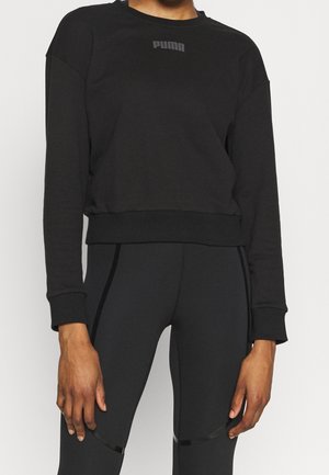 Persona con sudadera corta negra de manga larga Puma y leggings negros ajustados con detalles reflectantes sutiles.