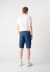 Mørkeblå denimshorts, litt falmet, med vanlig passform. Hvit t-skjorte med korte ermer. Hvite joggesko med lyse såler og ribbestrikkede sokker.
