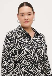 Black and white shirt featuring a swirling zebra print, made of smooth fabric, with a collar, button details, and long sleeves.