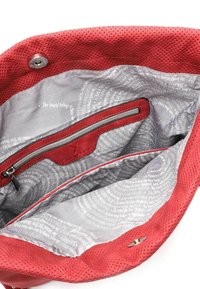 Intérieur d'un sac à main en tissu rouge perforé, avec une doublure argentée à motifs de texte et une poche zippée sur un côté.