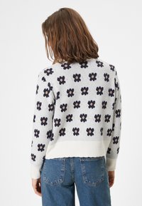 Sweter w kwiatowy wzór w jasnoszarym kolorze z granatowymi i beżowymi kwiatami. Żebrowane mankiety i dół, luźny krój, teksturowana dzianina, widok z tyłu.
