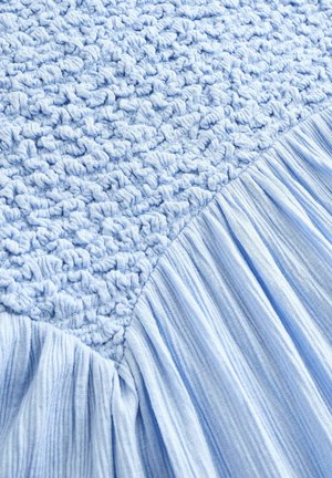 Vaalea sininen kangas, jossa on toisella puolella tekstuurillista virkkaa ja toisella puolella sileää, poimutettua kangasta, esitellen pehmeää, kerroksellista muotoilua.