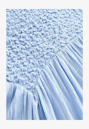 Vaalea sininen kangas, jossa on toisella puolella tekstuurillista virkkaa ja toisella puolella sileää, poimutettua kangasta, esitellen pehmeää, kerroksellista muotoilua.